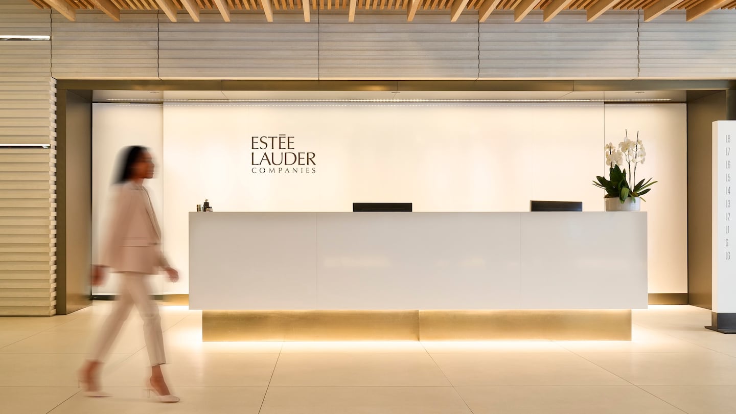 A figure walks from left to right in front of a light room and a concierge desk, behind which are written the words "Estée Lauder Companies".